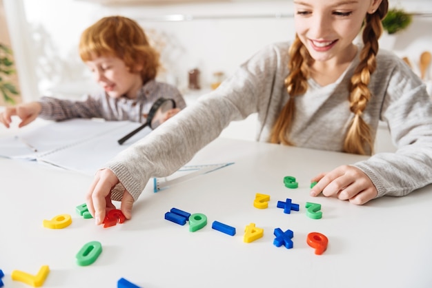 Begrijpelijke kleuren. Slim, zorgzaam positief meisje dat haar schattige gemberbroer wat rekenkunde leert terwijl ze speciale kleurrijke nummers gebruikt en ze in de juiste volgorde rangschikt