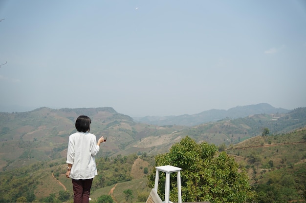 写真 ホット コーヒーを保持し、朝の山の景色を見て女性の背後にあります。