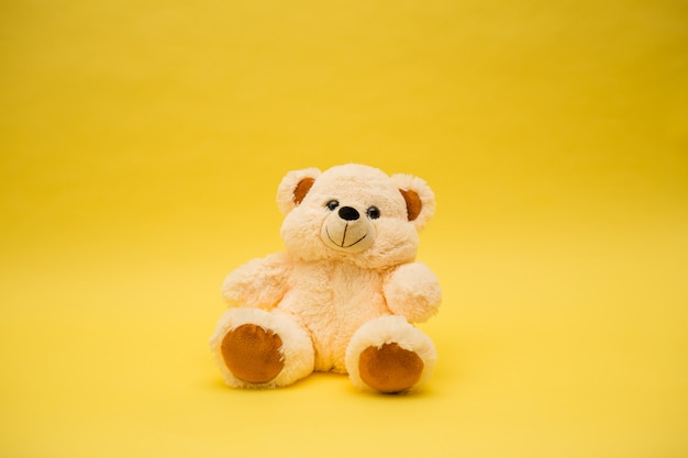 Beige bear toy on a yellow isolated background with a copy of the space