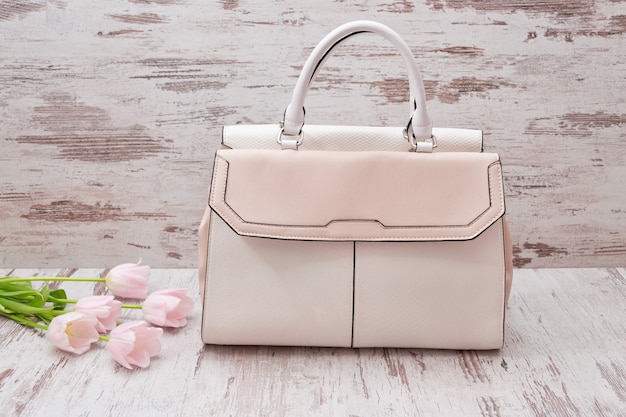 Beige big bag on a wooden surface, pink tulips. Fashionable concept.