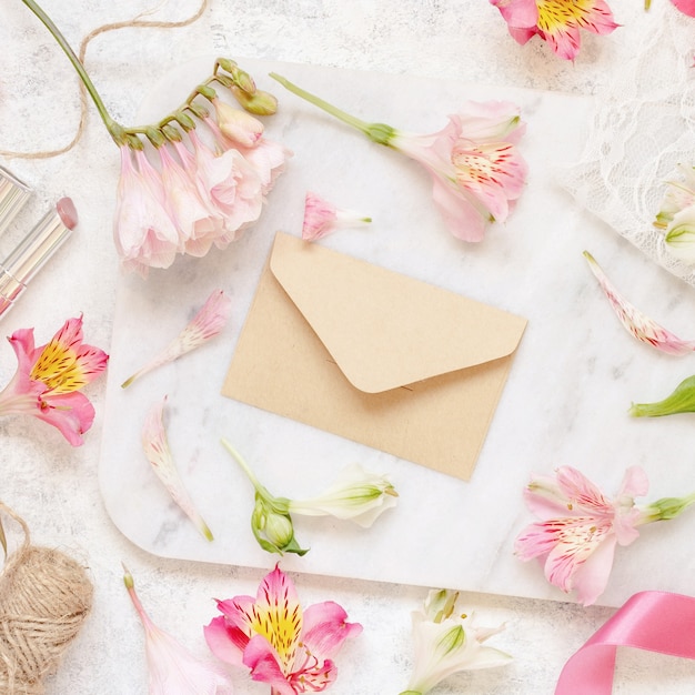 Beige envelope on a white table between pink flowers  top view