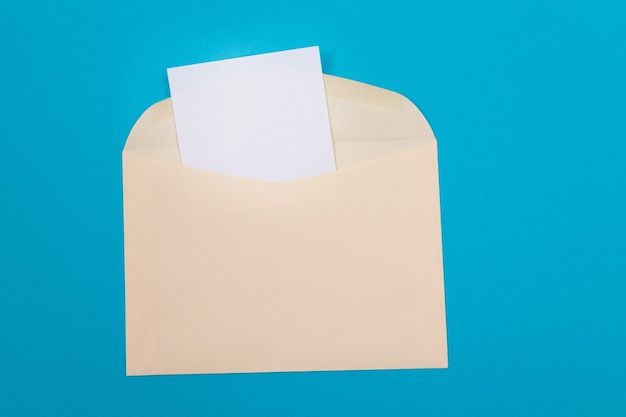 Beige envelope with blank white sheet of paper inside lying on blue background  mock up with copy sp...