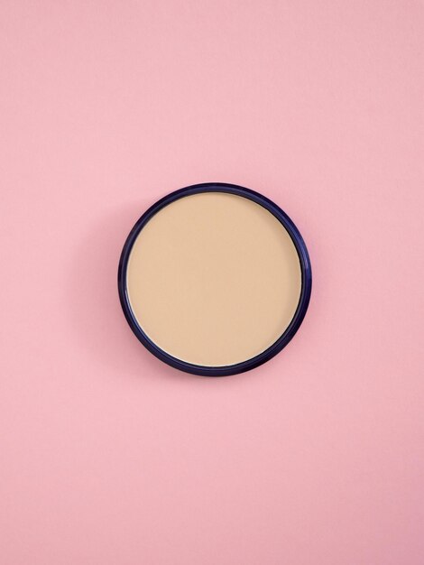 Foto polvere di concealer facciale beige vista superiore di polvere per viso nudo in scatola rotonda su sfondo di carta rosa prodotto di trucco cosmetico di moda bronzer e consistenza di concealer per una carnagione perfetta spazio di copia