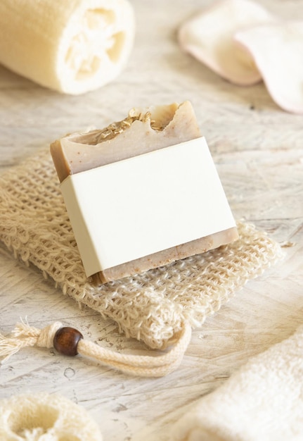 Beige handmade soap bar with blank label on soap saver bag on wooden table packaging mockup