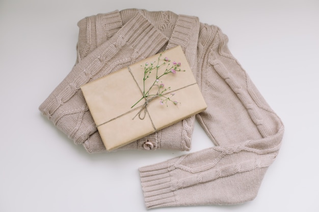 Beige knitted sweater with a gift in craft paper top view with copyspace