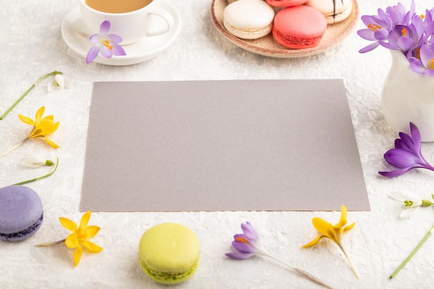 Beige paper sheet mockup with spring snowdrop crocus flowers and multicolored macaroons on gray concrete background side view copy space