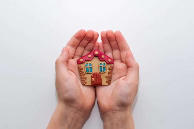 Beige plasticine house in the hands of a child on a white background