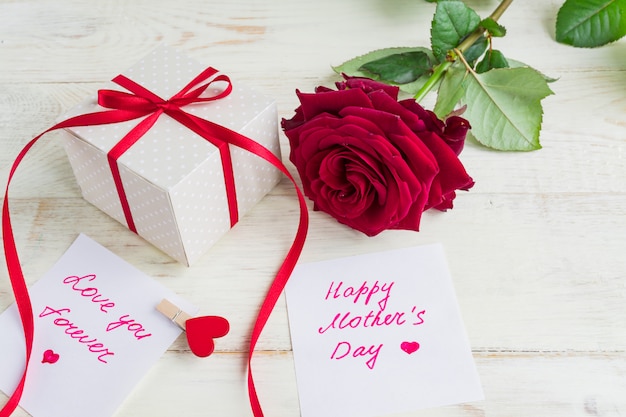 Beige polka dot gift box with red ribbon bow and bautiful red roses on wooden background. Greeting card for Mother's day