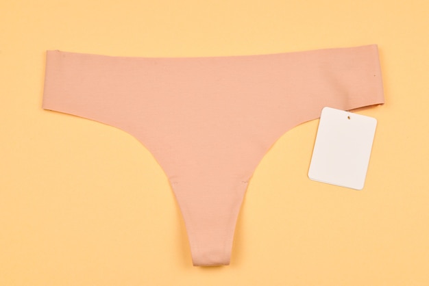 Beige seamless panties with tag  on beige background. Space for text or design.