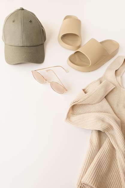 Beige slippers top sunglasses cap on white table Female fashion cloth and accessory concept Neutral dusty colour