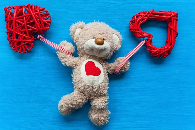 Beige, teddy bear lies on a turquoise table and holds a heart. Bear with a heart.