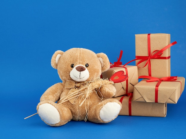 Beige teddy bear and a stack of boxes wrapped in brown kraft paper and tied with a red ribbon