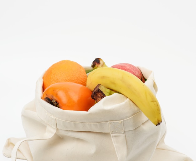 Beige textile bag with fresh fruits on a white surface,  zero wast