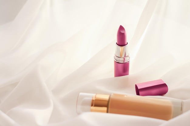 beige tonal cream bottle makeup fluid foundation base and pink lipstick on silk background cosmetics products as luxury beauty brand holiday design