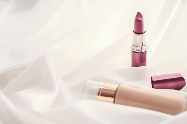 beige tonal cream bottle makeup fluid foundation base and pink lipstick on silk background cosmetics products as luxury beauty brand holiday design