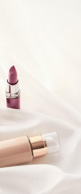 beige tonal cream bottle makeup fluid foundation base and pink lipstick on silk background cosmetics products as luxury beauty brand holiday design