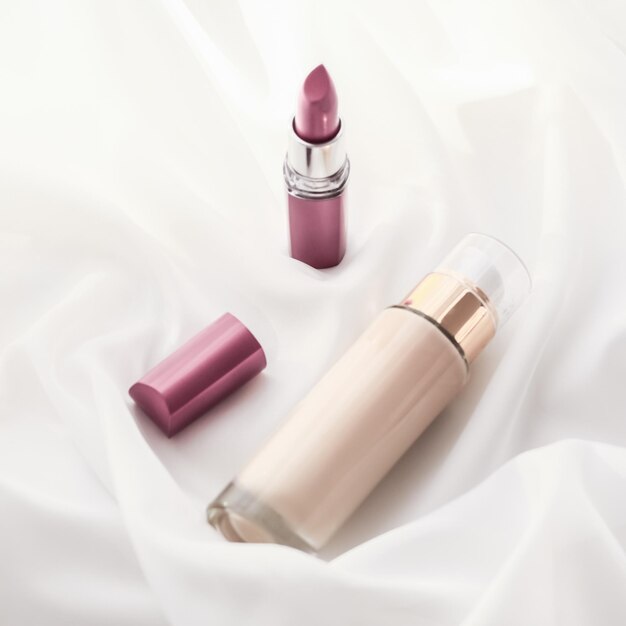 Beige tonal cream bottle makeup fluid foundation base and pink lipstick on silk background cosmetics products as luxury beauty brand holiday design