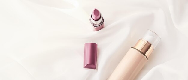 Beige tonal cream bottle makeup fluid foundation base and pink lipstick on silk background cosmetics products as luxury beauty brand holiday design