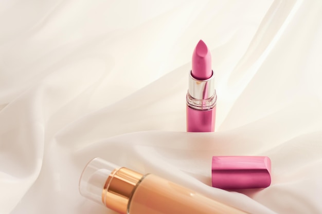 beige tonal cream bottle makeup fluid foundation base and pink lipstick on silk background cosmetics products as luxury beauty brand holiday design