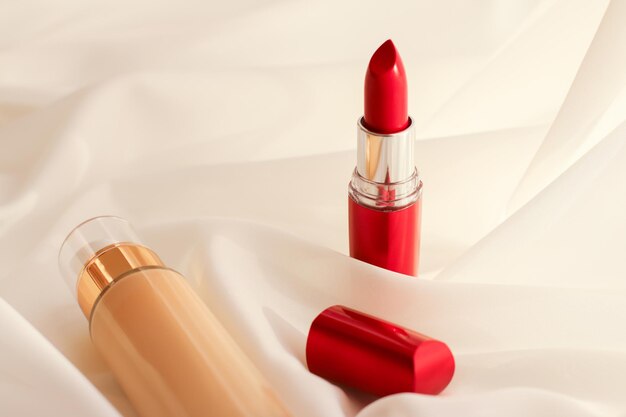 Beige tonal cream bottle makeup fluid foundation base and red lipstick on silk background cosmetics products as luxury beauty brand holiday design