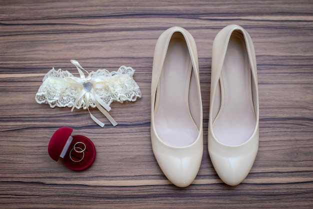 Beige trouwschoenen witte bruids kousenband en trouwringen in rode doos op houten achtergrond