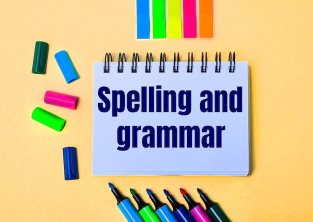 ベージュの壁に、SPELLING AND GRAMMARという言葉が書かれたノート、明るいフェルトペンとステッカー