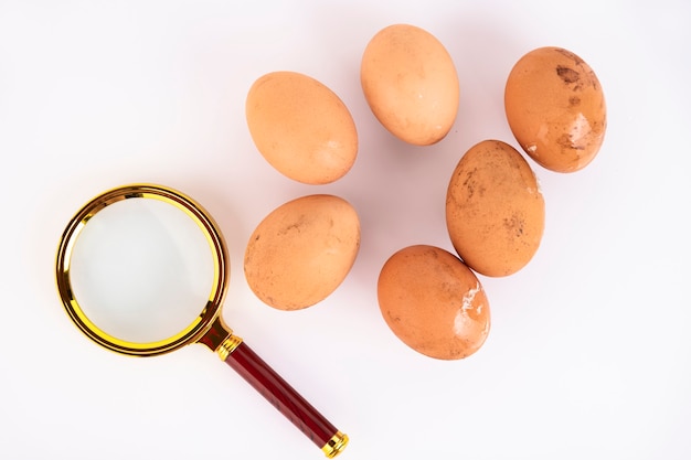 Beige, wild chicken eggs and a magnifying glass on a white background. Selective focus. Copy space.