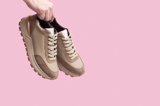 Beige women's leather sneakers in hand on pink background