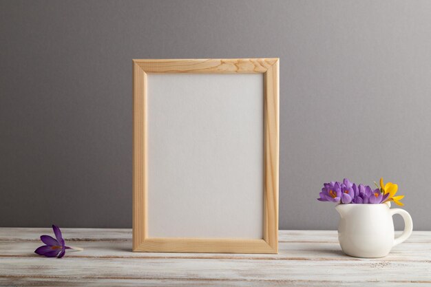 Beige wooden frame mockup with snowdrop crocus flowers on gray\
paper background still life copy space