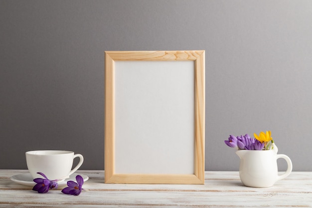 Beige wooden frame mockup with snowdrop crocus flowers and white coffee cup on gray paper background still life copy space