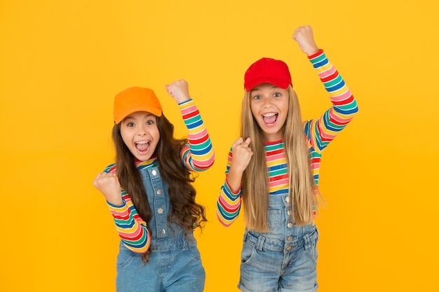 Being happy and victorious little girls making victory gestures on yellow background cute small winners enjoying victory together happy children celebrating victory or success victory and triumph