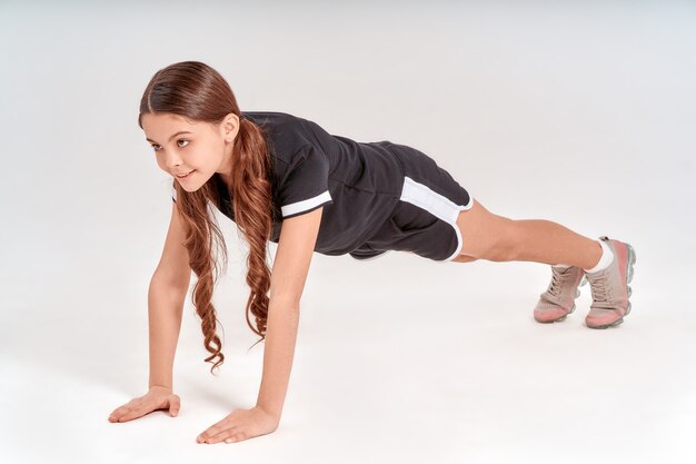 板に立っているスポーツウェアのキュートで幸せな10代の少女の身体的にアクティブな全長であること