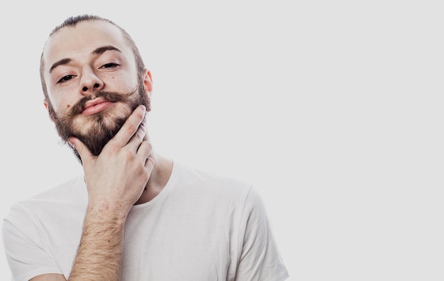 Being serious Concentrated bearded man wearing a white shirt and an earring and touching his chin while thinking