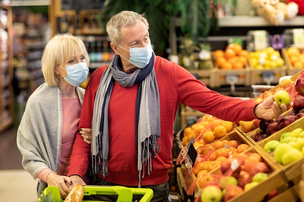 Bejaard echtpaar met gezichtsmaskers die vers fruit kiezen