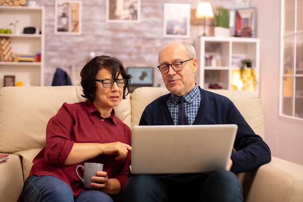 Bejaard oud echtpaar dat moderne laptop gebruikt om met hun kleinzoon te chatten. Grootmoeder en grootvader met behulp van moderne technologie