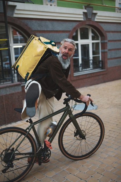 Foto bejaarde bezorger met fiets maken grappig gezicht genieten van werken