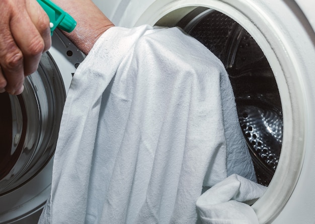 Bejaarde dame ontsmet een witte doek, met een groene spray met een ontsmettingsmiddel, voordat ze in de wasmachine gaat