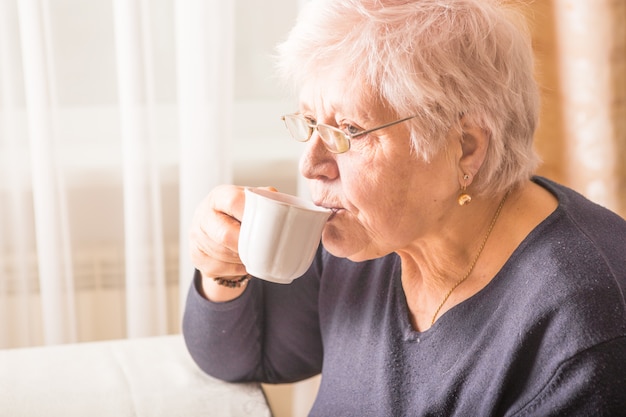 Bejaarde die hete drank thuis drinkt. Senior gepensioneerde vrouw met kopje koffie in hun handen