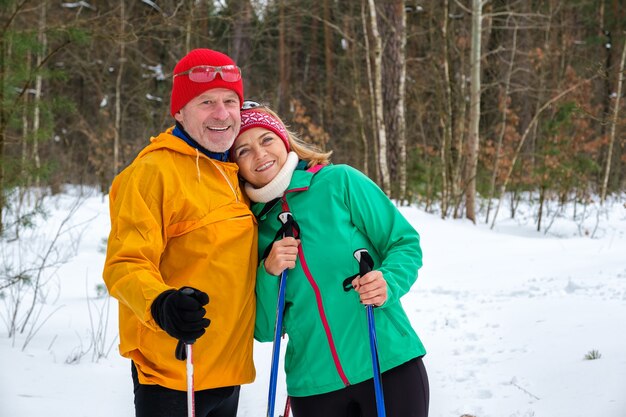 Bejaarde echtpaar wandelen met nordic walking-stokken in besneeuwde winterpark