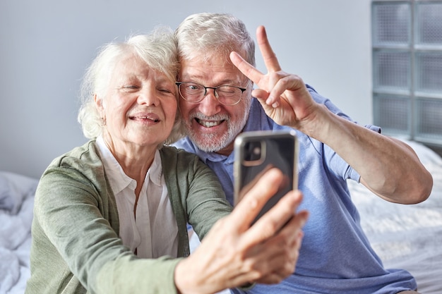 Bejaarde echtpaar zittend op een bank nemen foto op smartphone, poseren voor de camera van de telefoon, genieten van tijd in het weekend. familie, technologie, leeftijd en mensenconcept