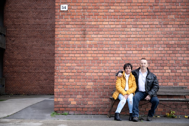 Bejaarde echtpaar zittend op een bankje in de buurt van een bakstenen muur