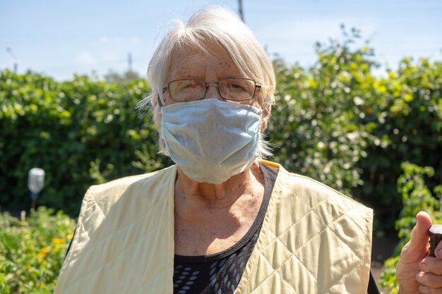 Bejaarde in haar tuin die gezichtsmasker draagt