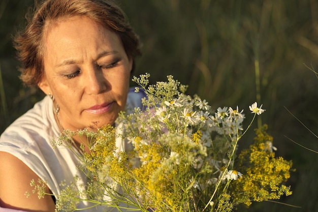 Bejaarde maar nog steeds aantrekkelijke aziatische vrouw die de geur van een wilde bloem inademt in een stralende zon