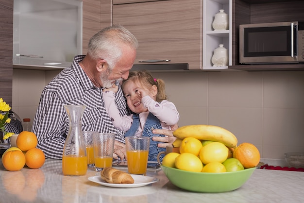 Bejaarde man en zijn schattige kleindochter vers sinaasappelsap drinken en plezier in een keuken