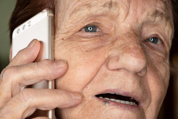 Bejaarde senior vrouw met goudkleurige telefoon naast haar oor, pratend - close-up detail