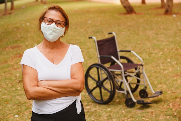 Bejaarde vrouw die met beschermend masker tegen covid met dwarsarmen glimlacht