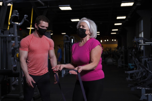 Bejaarde vrouw en haar persoonlijke trainer die medische maskers dragen tijdens gymnastiektraining