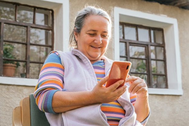 Bejaarde vrouw zitten, glimlachen en met behulp van haar smartphone