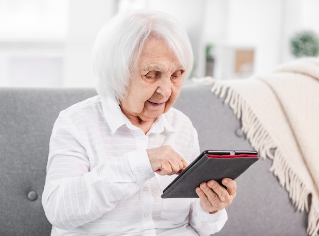 Bejaarde vrouw zittend met tablet op de bank en kijken naar het scherm