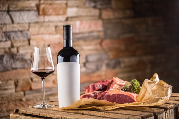 Beker en een fles rode wijn en rauwe biefstuk op houten tafel.